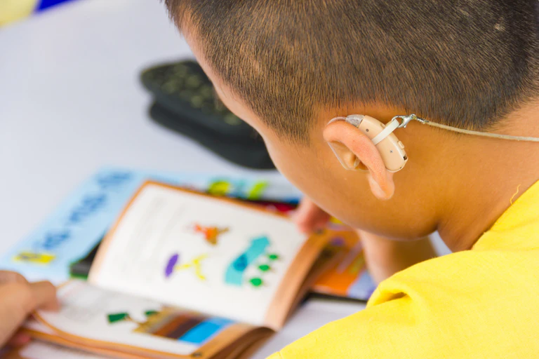 A boy with a hearing aid reading a book
