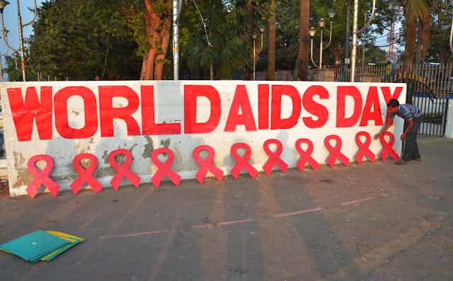 Man arrange red ribbon symbols in front of World AIDS Day mural.