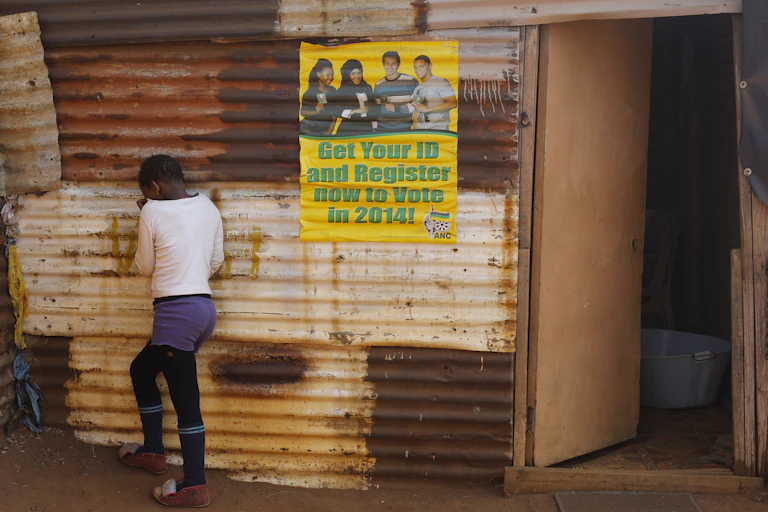 A child wearing a white jersey, purple shorts and long black socks outside her family shack