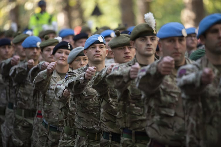 Soldiers walk in step wearing camouflage uniforms and berets