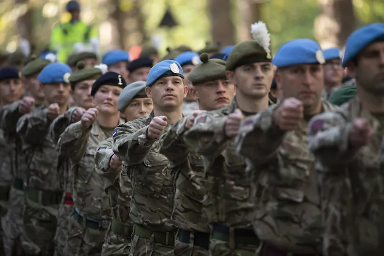 Soldiers walk in step wearing camouflage uniforms and berets