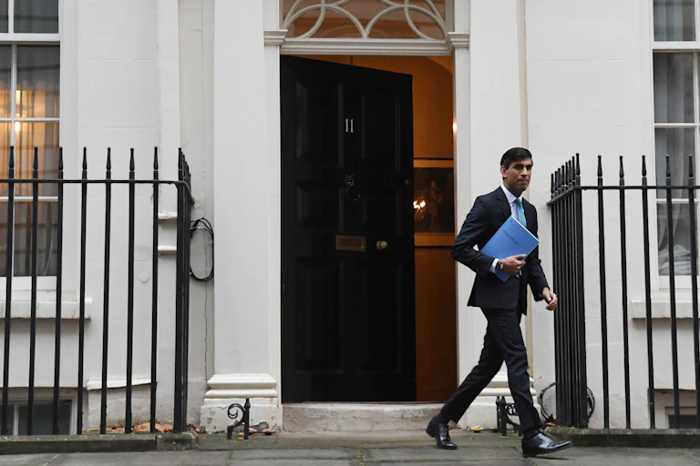 Rishi Sunak exits No.11 carrying a blue document labelled the spending review