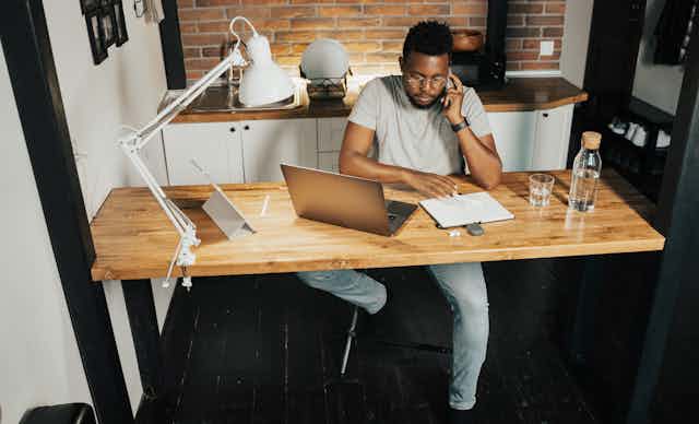 A man sits at his kitchen counter with his laptop and a notepad.