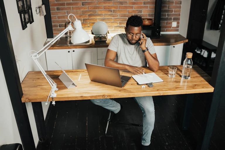 A man sits at his kitchen counter with his laptop and a notepad.
