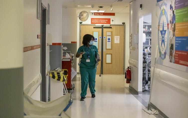 A woman wearing scrubs stands in a hospital corridor.