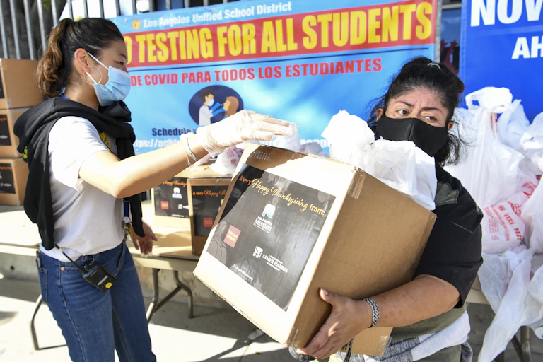 A woman in a mask carries a box of donated food