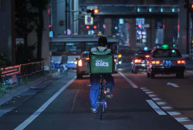 Food delivery rider cycles down busy city street at night