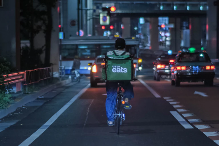 Food delivery rider cycles down busy city street at night