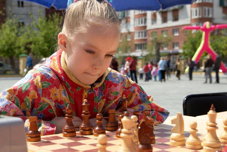 A girl plays chess in a public park.