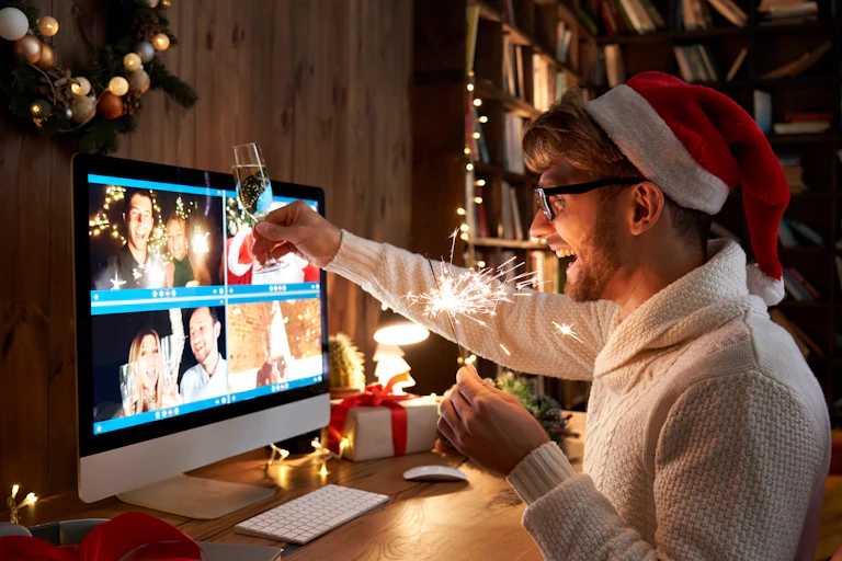 Young man wearing Christmas hat drinking champagne holding sparkler talking to friends on virtual zoom video call.
