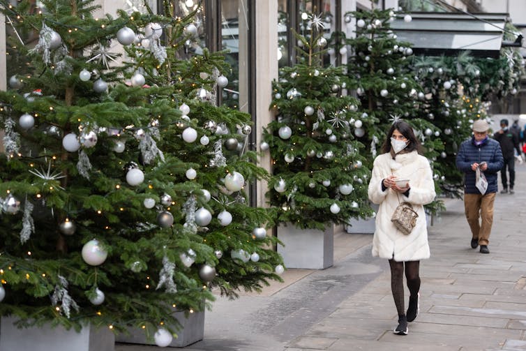 A woman walks past a display of Christmas trees.