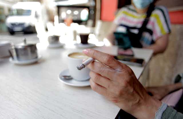 A hand holding a cigarette with pink nail varnish at a breakfast table in A Coruña Spain, 2020