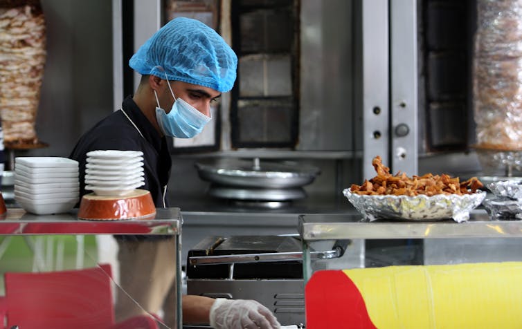 Man working in kebab shop, wearing hair net, gloves and mask.
