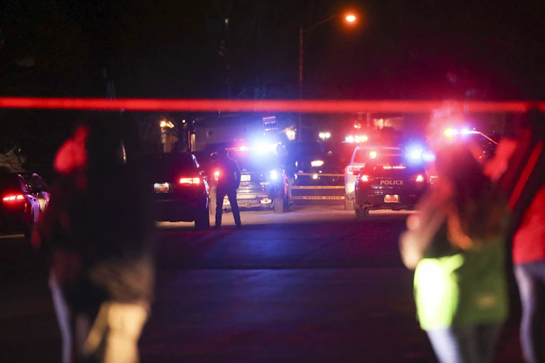 Two women in foreground watch as police investigate a shooting in Utah, January 2020.