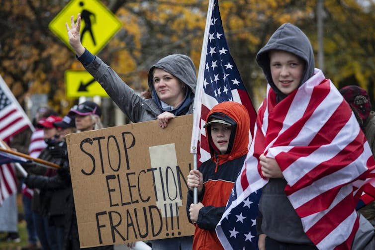 A woman and two children dressed in rain jackets hold up a Stop Election Fraud sign