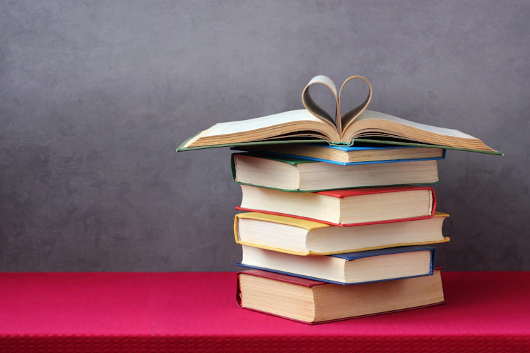 Pila de libros. El superior abierto con varias hojas formando un corazón.