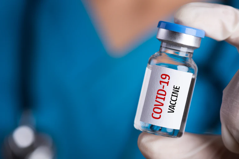 A gloved hand holding a vial labelled COVID-19 vaccine