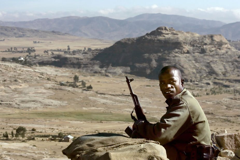 A dressed in green military and armed with an AK-47 rifle keeps watch over a mountanious area 
