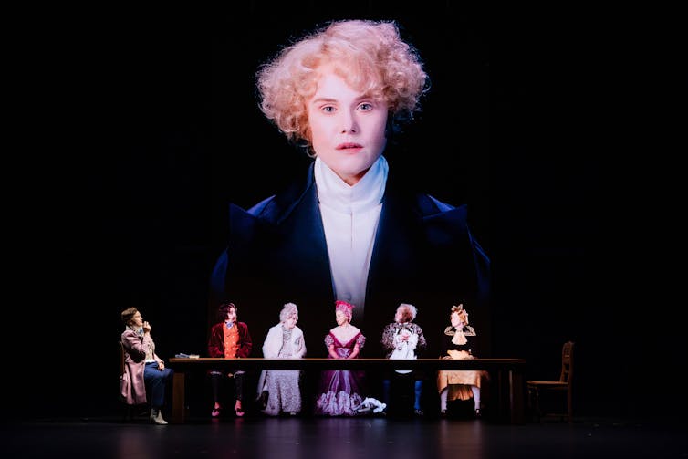 Woman projected on screen behind women seated onstage.