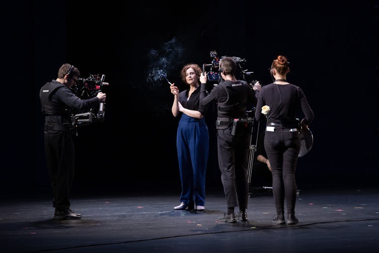 Woman smoking, surrounded by actors as reporters.