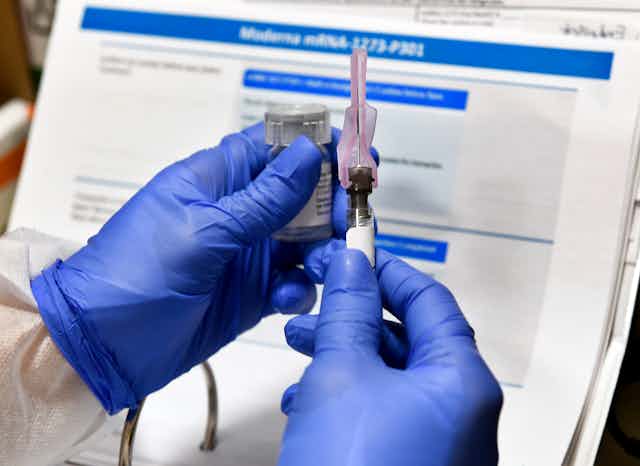 Gloved hands holding a syringe and vaccine vial