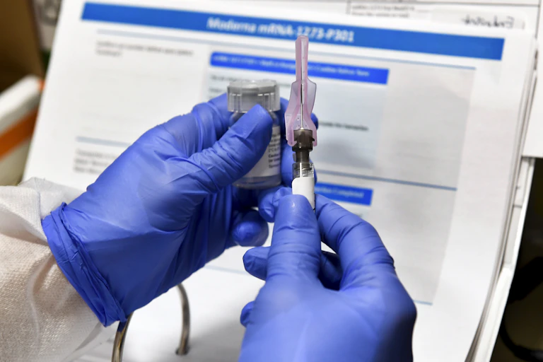 Gloved hands holding a syringe and vaccine vial