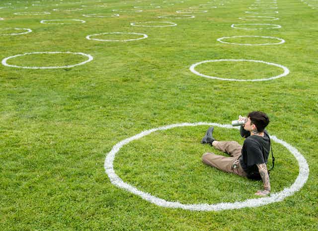 A man sits on the grass in a white circle, with dozens of empty white circles on the expanse of grass in the background