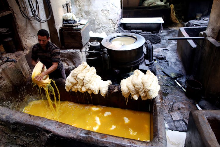 A worker removes a bundle of cotton yarn from a stone trough filled with yellow dye.