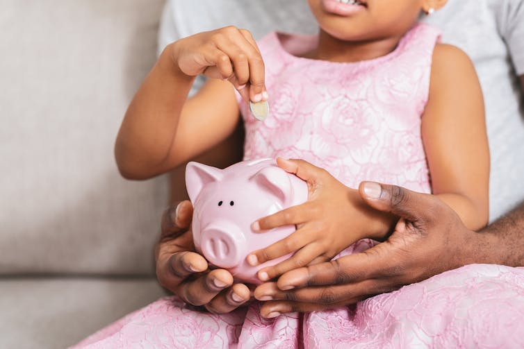 A child puts a coin in a piggy bank.