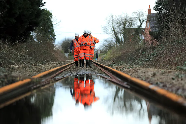 Three workers inspect a flooded railway track.
