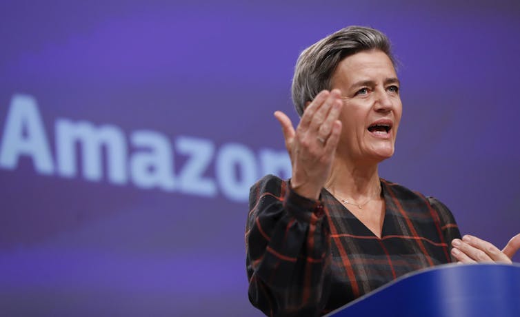 A woman gestures while speaking in front of an Amazon sign.