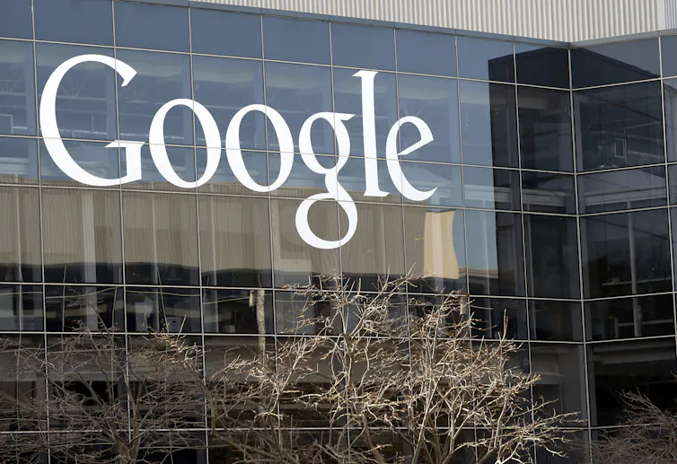 The Google logo on a glass building with trees in front.