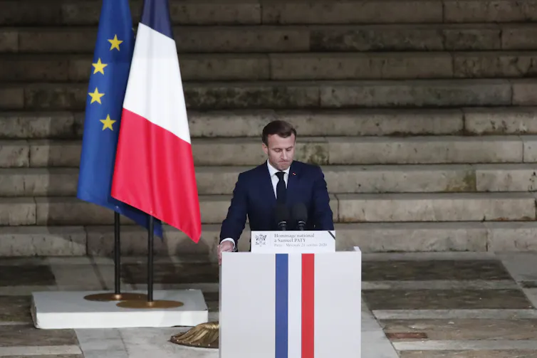 Man at lectern in front of French and EU flags.