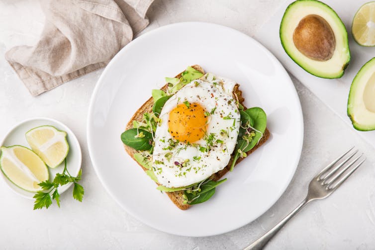 Toast with avocado, spinach and fried egg, top view.