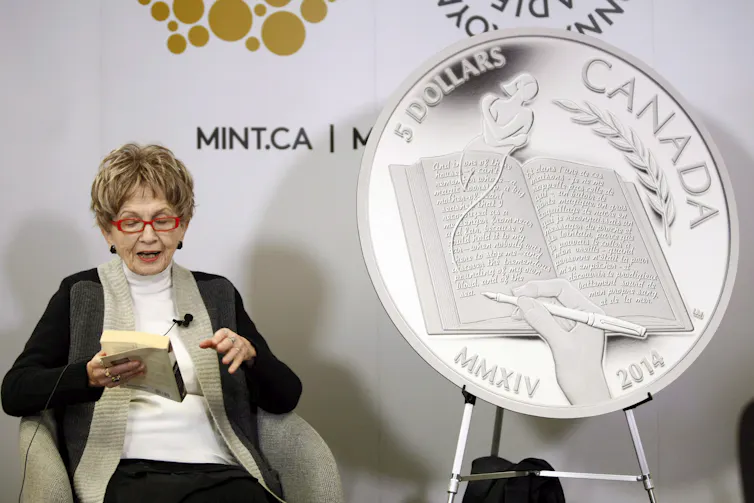 The author Alice Munro reads from her book while sitting next to a large replica of the $5 coin celebrating her achievements.