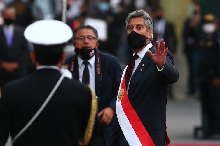 Sagasti, wearing a face mask and a presidential sash, waves at the camera