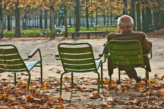 un hombre mayor en un parque en otoño sentado en una silla de espaldas