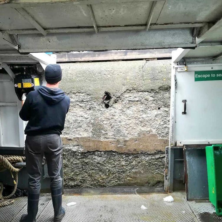 A man in fishing gear looks at a cement wall
