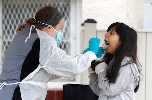 A healthcare worker swabs the back of a young girls throat for a rapid COVID-19 test