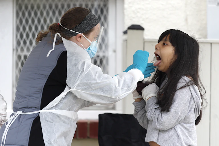 A healthcare worker swabs the back of a young girls throat for a rapid COVID-19 test