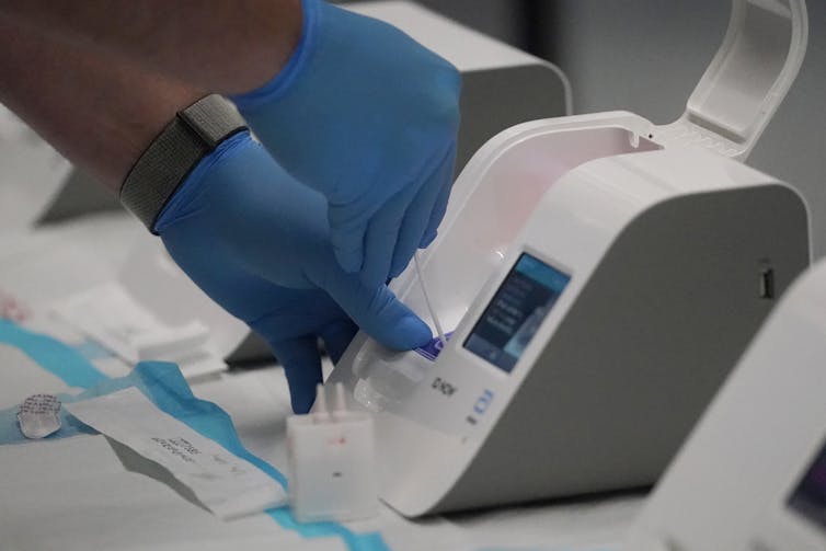 A healthcare worker placing a sample into a the small Abbott ID Now processing machine.