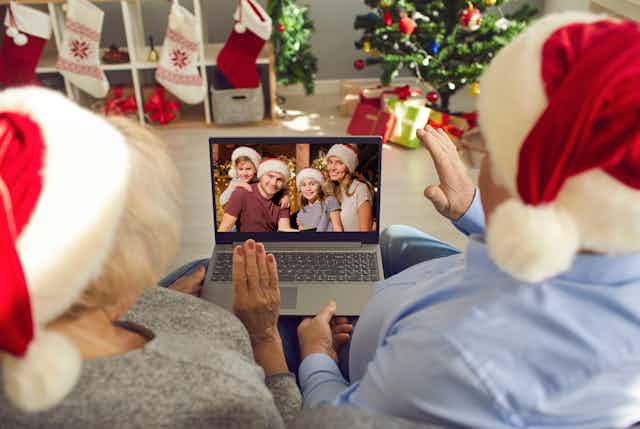 Two people in Santa hats wave at a family in Santa hats on a laptop screen.