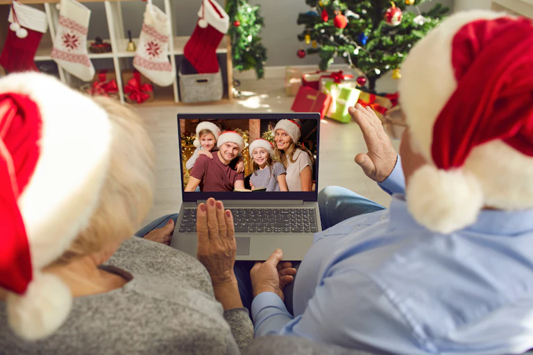 Two people in Santa hats wave at a family in Santa hats on a laptop screen.