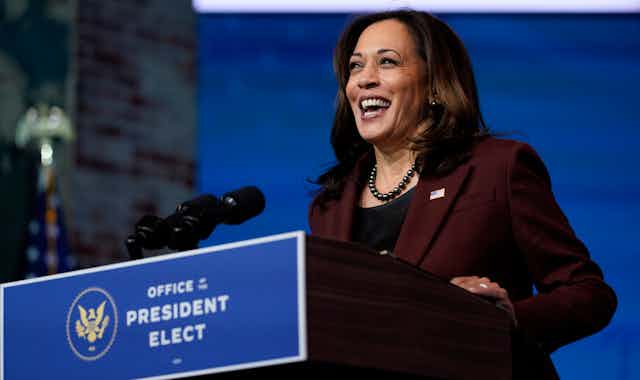 Kamala Harris laughs while standing at a podium labelled Office of the President Elect.
