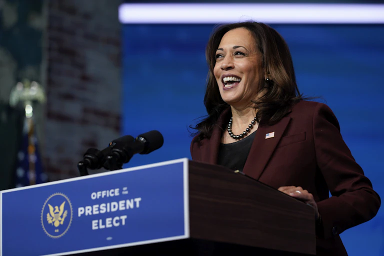 Kamala Harris laughs while standing at a podium labelled Office of the President Elect.