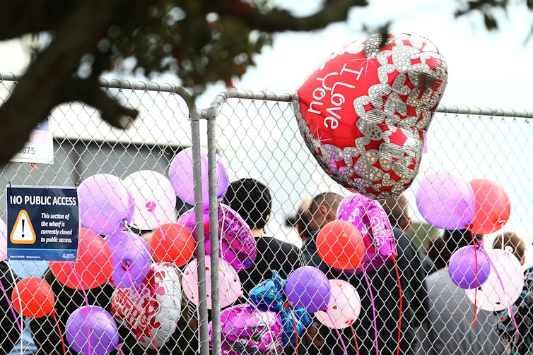 A heart shaped balloon saying I love you shown tied to
a fence with other balloons.