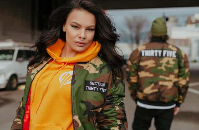 A woman and man stand in camo-style bomber jackets.