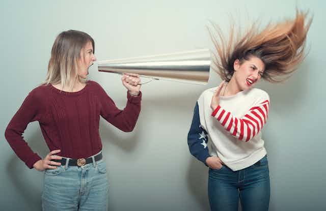 young woman yells thru bullhorn at another woman whose hair is blown back