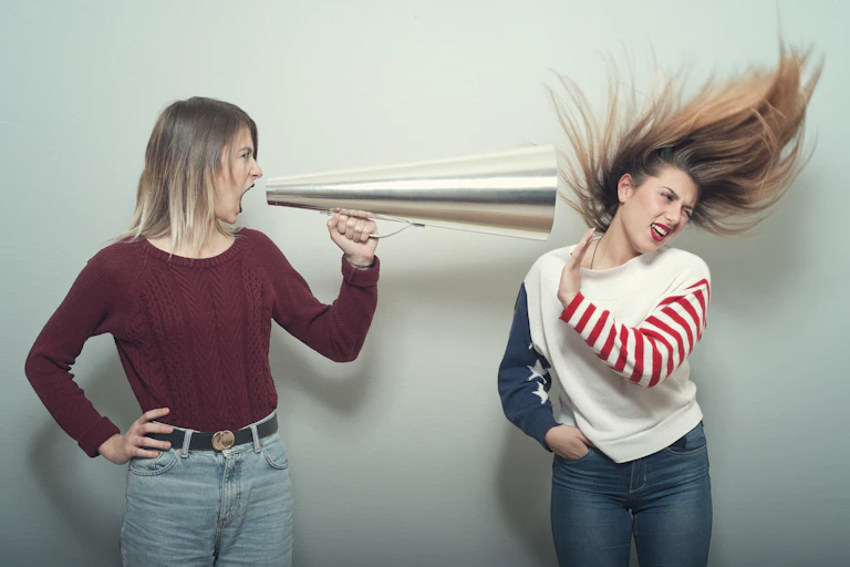 young woman yells thru bullhorn at another woman whose hair is blown back