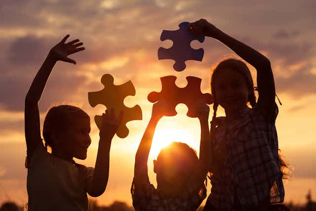 A silhouette of three school children holding up large puzzle pieces against a sunset
